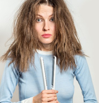 Funny woman with messy hair holding straightening irons